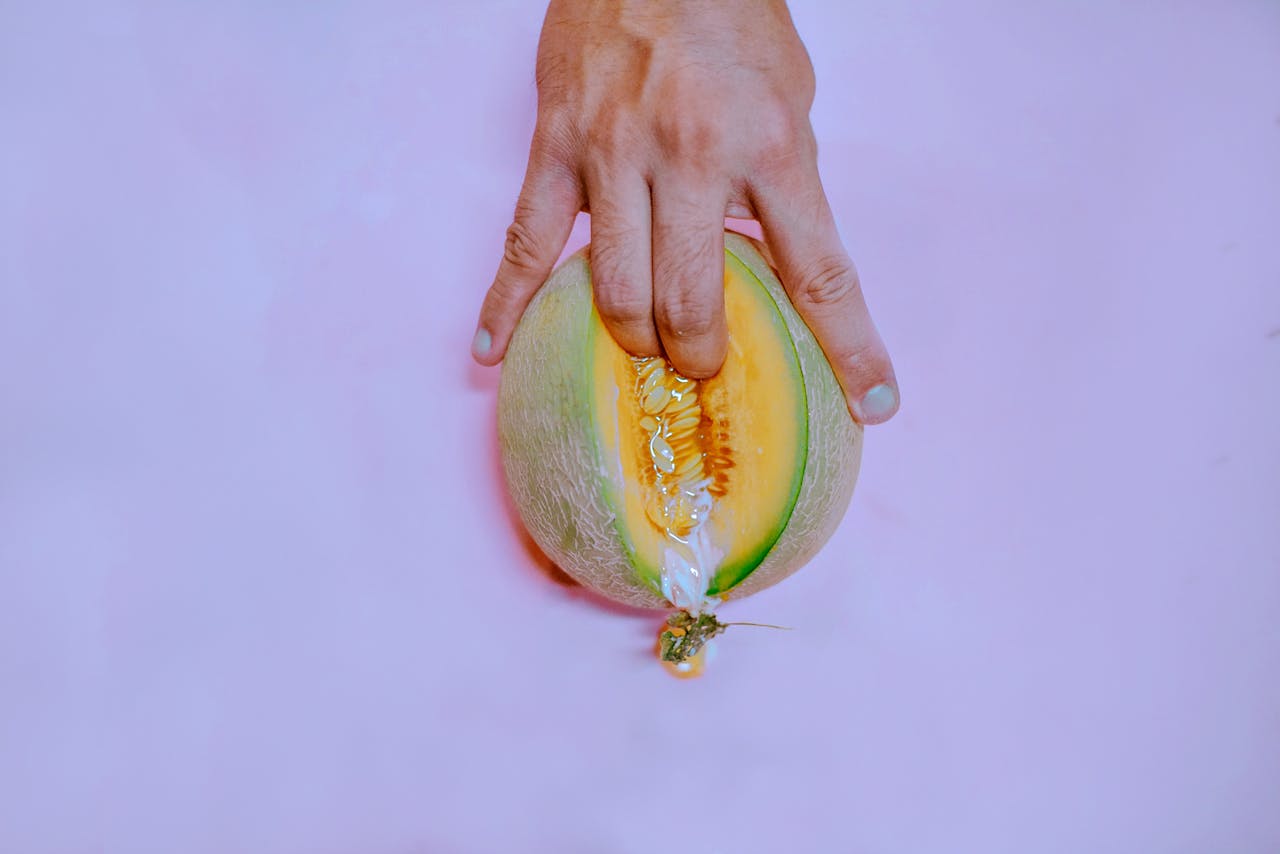 about-us-01 A hand gently touches a ripe melon on a pastel pink backdrop, creating a vivid and conceptual image.