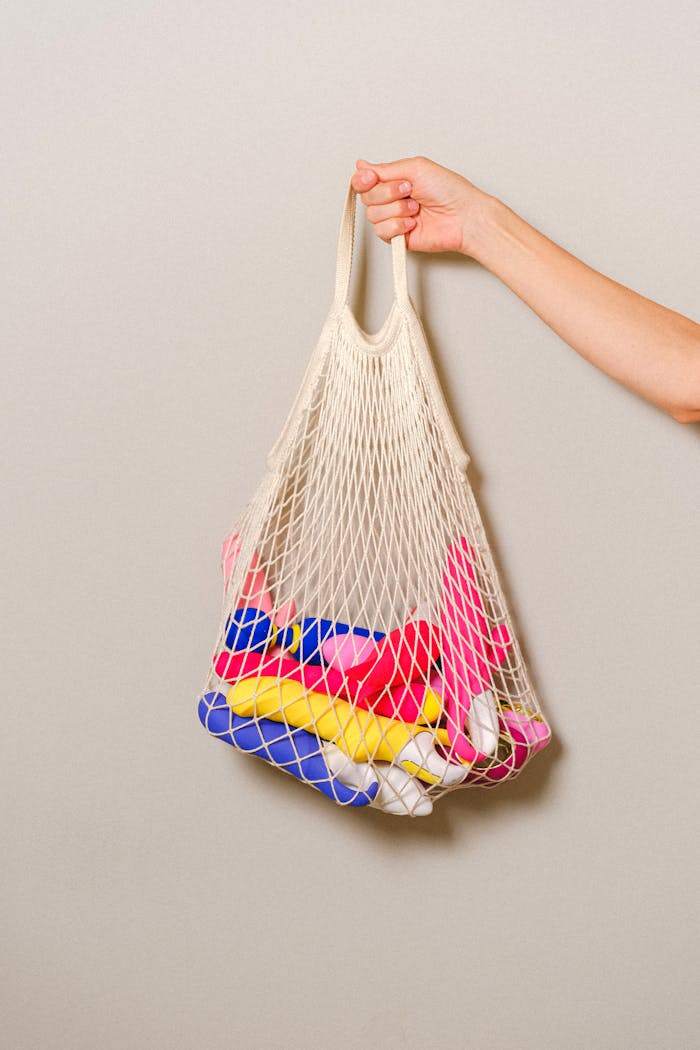 about-us-01 A mesh bag filled with colorful silicone sex toys held by an adult's hand against a neutral background.